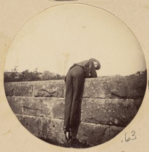 Homme avec un chapeau penché sur un mur de pierre